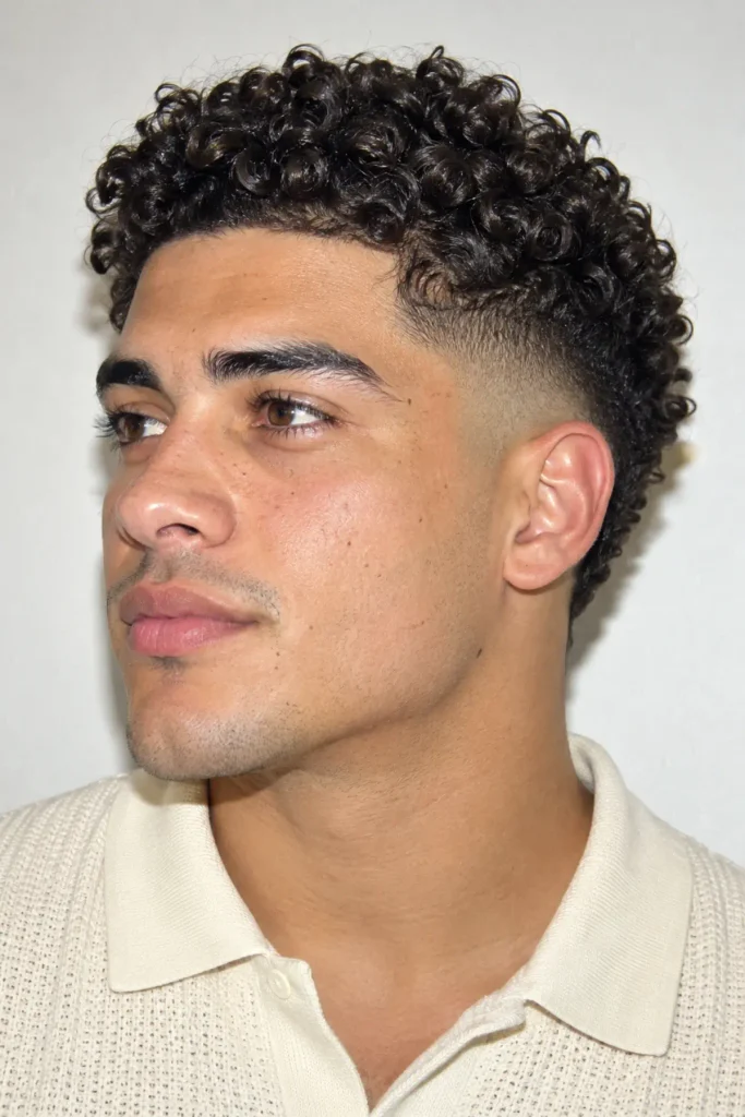 Man with a mid burst fade and tight curly hair, showing defined springy curls on top and clean faded sides around the ears.